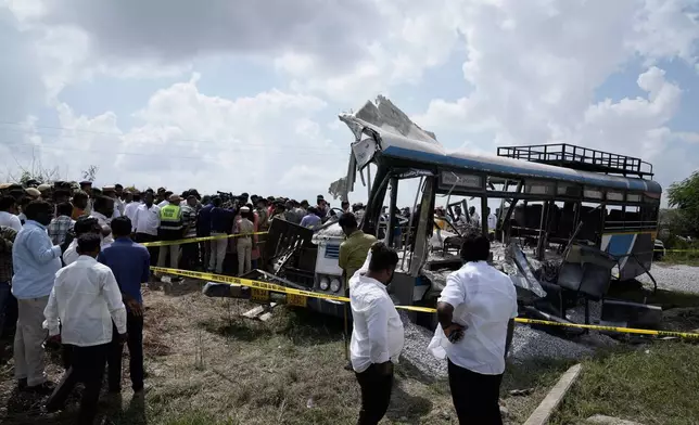 CAPTION CORRECTS THE LOCATION - People stand next to the passenger bus after a truck loaded with concrete stone chips rammed into it at Chevella in southern state of Telangana, India, Monday, Nov. 3, 2025. (AP Photo/Mahesh Kumar A.)