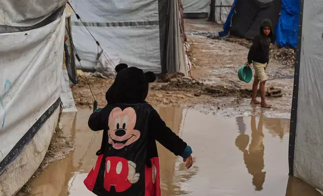 FILE - A Palestinian walks a mud puddle at a temporary tent encamp flooded by A heavy rainfall in Deir al-Balah, central Gaza Strip, Nov. 25, 2025. (AP Photo/Abdel Kareem Hana, File)