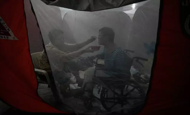 Judy Bertuso, left, feeds her husband Apollo inside a tent at an evacuation center as Typhoon Fung-wong enters the country on Sunday, Nov. 9, 2025 in Quezon city, Philippines. (AP Photo/Aaron Favila)