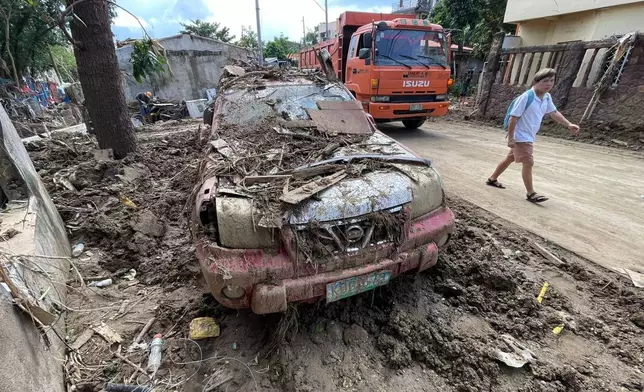 A man passes by a debris laden car as residents return to their flood damaged homes in Bacayan, Cebu province, central Philippines on Friday Nov. 7, 2025 after Typhoon Kalmaegi devastated the province and claimed lives. (AP Photo/Jacqueline Hernandez)