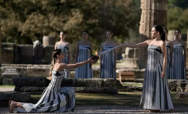 Actress Mary Mina, right, playing the role of high priestess performs passes the flame during a rehearsal ahead of the flame lighting for the Milan Cortina 2026 Winter Olympics, at the Ancient Olympia site, Greece, Monday, Nov. 24, 2025. (AP Photo/Thanassis Stavrakis)