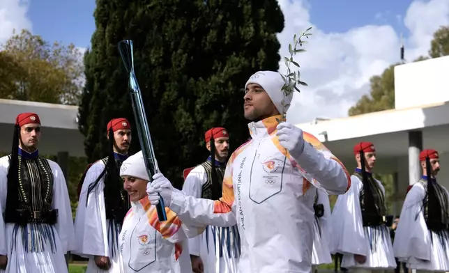 Greek rower Petros Gaidatzis, right, and former Italy's Cross Country skier Stefania Belmondo start the torch relay after the ceremony of the flame lighting for the Milan Cortina 2026 Winter Olympics, at the archaeological museum of Olympia, Greece, Wednesday, Nov. 26, 2025. (AP Photo/Petros Giannakouris)