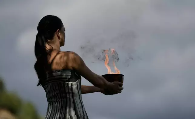 Actress Mary Mina, playing the high priestess holds a pot with the flame during a rehearsal ahead of the flame lighting for the Milan Cortina 2026 Winter Olympics, at the Ancient Olympia site, Greece, Monday, Nov. 24, 2025. (AP Photo/Petros Giannakouris)