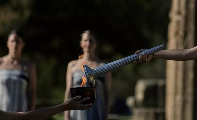 Actress Mary Mina, right, playing the high priestess light lights the flame during a rehearsal ahead of the flame lighting for the Milan Cortina 2026 Winter Olympics, at the Ancient Olympia site, Greece, Monday, Nov. 24, 2025. (AP Photo/Petros Giannakouris)