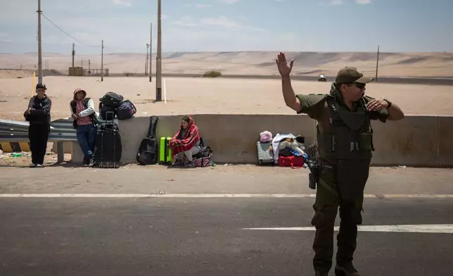 A police officer directs traffic at the Chacalluta border crossing point in Arica, Chile, Friday, Nov. 28, 2025, as migrants wait to cross into Peru. (AP Photo/Ibar Silva)