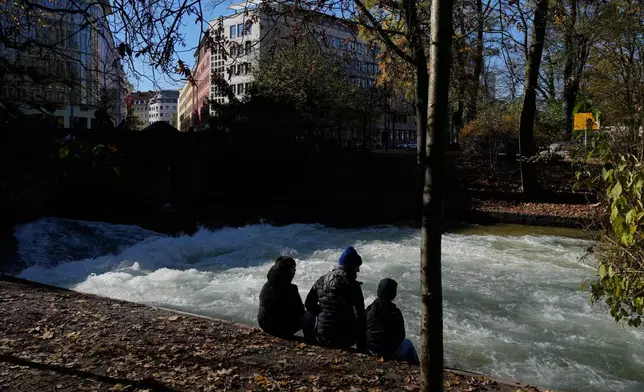 People sit at the Eisbach, where the famous wave usually forms, in Munich, Germany, Wednesday, Nov. 5, 2025. (AP Photo/Matthias Schrader)