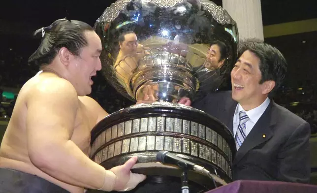 FILE - Grand champion Asashoryu of Mongolia, left, receives the Prime Minister's Cup from Chief Cabinet Secretary and soon-to-be Premier Shinzo Abe at Tokyo's Ryogoku Sumo Arena on Sept. 24, 2006. (Kyodo News via AP, File)