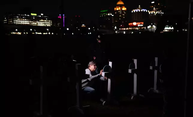 Dianne Graves writes on a heart-shaped placard attached to a cross during a vigil honoring the victims of a deadly UPS plane disaster, at the Great Lawn in Louisville, Ky., Friday, Nov. 7, 2025. (AP Photo/Jon Cherry)