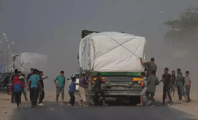 Palestinians rush toward trucks carrying aid as they drive through Deir al-Balah in central Gaza, Sunday, Nov. 9, 2025. (AP Photo/Jehad Alshrafi)
