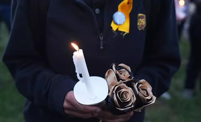 An attendee holds a candle and flowers during a vigil Thursday, Nov. 6, 2025, in Louisville, Ky., after a UPS plane crashed at Louisville Muhammad Ali International Airport. (AP Photo/Darron Cummings)