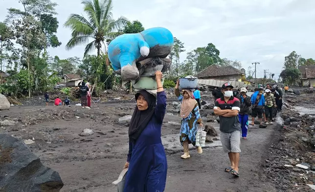 People carry their belongings as they evacuate their homes at a village affected by the eruption of Mount Semeru in Lumajang, East Java, Indonesia, Thursday, Nov. 20, 2025. (AP Photo/Wawan Sugiarto)