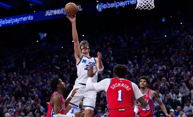 Orlando Magic's Franz Wagner, top, shoots the ball over Philadelphia 76ers' Justin Edwards, left, and Andre Drummond (1) during the first half of an NBA Cup basketball game, Tuesday, Nov. 25, 2025, in Philadelphia. (AP Photo/Chris Szagola)