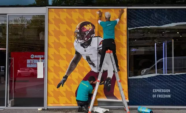 A worker pastes a poster on the facade of the renovated Santiago Bernabeu stadium ahead of an NFL regular-season game between the Washington Commanders and the Miami Dolphins in Madrid, Spain, Tuesday, Nov. 11, 2025. (AP Photo/Bernat Armangue)