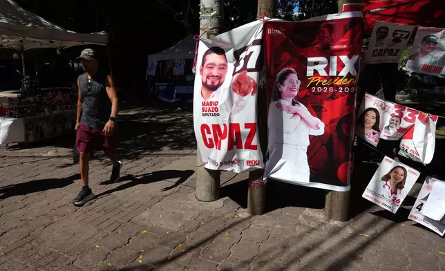 A man walks past a stand with campaign posters of ruling party presidential candidate Rixi Moncada in Tegucigalpa, Honduras, Thursday, Nov. 27, 2025 prior to general elections. (AP Photo/Moises Castillo)