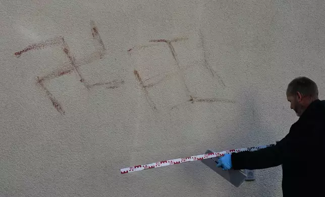 Criminal experts measure swatsikas at a house in Hanau, Germany, Thursday, Nov. 6, 2025, the day after a a person painted with blood swastikas on cars and houses. (AP Photo/Michael Probst)