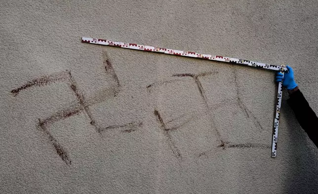 Criminal experts measure swastikas at a house in Hanau, Germany, Thursday, Nov. 6, 2025, the day after a a person painted with blood swastikas on cars and houses. (AP Photo/Michael Probst)
