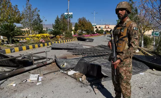 An Army soldier stands guard next to damages at the main gate of an army-run cadet college that was assaulted by militants on Monday, in Wana, a city in the northwestern Pakistani district South Waziristan bordering with Afghanistan, Thursday, Nov. 13, 2025. (AP Photo/Ahsan Shahzad)