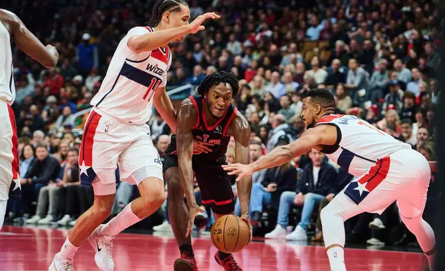 Toronto Raptors' Immanuel Quickley (centre) drives through Washington Wizards' Kyshawn George (left) and CJ McCollum (right) during first half NBA basketball action in Toronto, Friday, Nov. 21, 2025. (Sammy Kogan/The Canadian Press via AP)