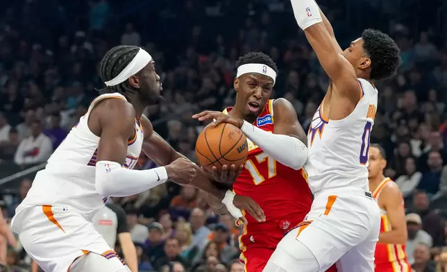 Atlanta Hawks forward Onyeka Okongwu, center, gets double teamed by Phoenix Suns center Mark William, left, and Phoenix Suns forward Ryan Dunn during the first half of an NBA basketball game in Phoenix, Sunday, Nov. 16, 2025. (AP Photo/Darryl Webb)