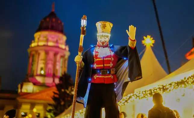 An artist on stilts performs on the illuminate Christmas Market at the Gendarmen Markt square in Berlin, Germany, Monday, Nov. 24, 2025. (AP Photo/Markus Schreiber)
