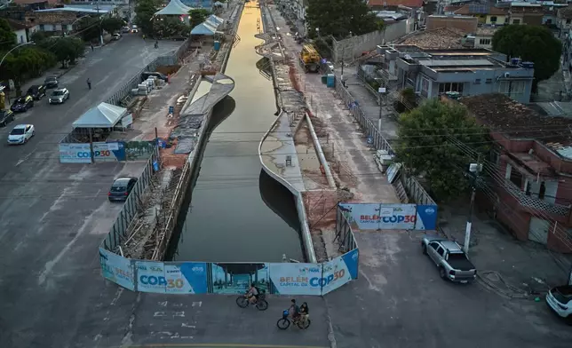 FILE - People ride bikes near signage for the upcoming COP30 U.N. Climate Summit in Belem, Brazil, March 23, 2025. (AP Photo/Jorge Saenz, File)