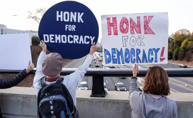 Protesters hold signs amidst the arrival of federal law enforcement, Tuesday, Nov. 18, 2025, in Charlotte, N.C. (AP Photo/Matt Kelley)