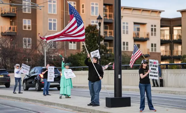 Protesters hold signs and flags amidst the arrival of federal law enforcement, Tuesday, Nov. 18, 2025, in Charlotte, N.C. (AP Photo/Matt Kelley)