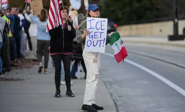 Protesters hold signs amidst the arrival of federal law enforcement, Tuesday, Nov. 18, 2025, in Charlotte, N.C. (AP Photo/Matt Kelley)
