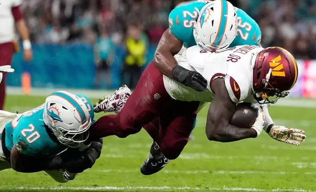 Washington Commanders wide receiver Deebo Samuel (1) is tackled by Miami Dolphins linebacker Jordyn Brooks (20) and linebacker Tyrel Dodson (25) during the first half of an NFL football game between the Washington Commanders and the Miami Dolphins in Madrid, Spain, Sunday, Nov. 16, 2025. (AP Photo/Bernat Armangue)