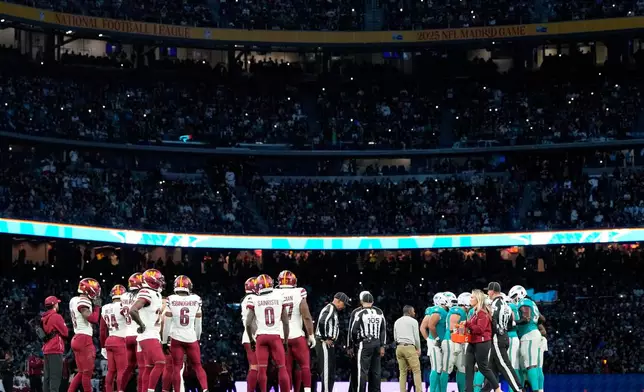 Washington Commanders, left, and Miami Dolphins players stand on the field during the second half of an NFL football game between the Washington Commanders and the Miami Dolphins in Madrid, Spain, Sunday, Nov. 16, 2025. (AP Photo/Bernat Armangue)