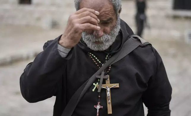 A worshipper makes the sign of the cross while wearing several crucifixes around his neck at the shrine of St. Charbel in the northern village of Annaya, Lebanon, Saturday, Nov. 15, 2025. (AP Photo/Hassan Ammar)
