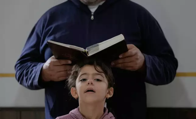 A girl gestures as her family attends Sunday Mass inside a room usually used as a residence for visiting bishops next to St. George Melkite Catholic Church, which was destroyed in an Israeli airstrike, in the town of Dardghaya, southern Lebanon, Sunday, Nov. 16, 2025. (AP Photo/Hassan Ammar)