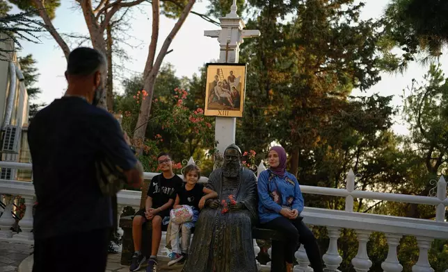 A Muslim family poses for a photo next to a statue of St. Charbel at the Our Lady of Lebanon shrine in Harissa, east of Beirut, Lebanon, Sunday, Nov. 9, 2025. (AP Photo/Hassan Ammar)