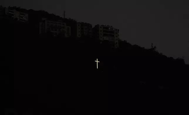 A cross glows on a hillside above residential buildings at dusk in the coastal town of Jounieh, north of Beirut, Lebanon, Sunday, Nov. 9, 2025. (AP Photo/Hassan Ammar)