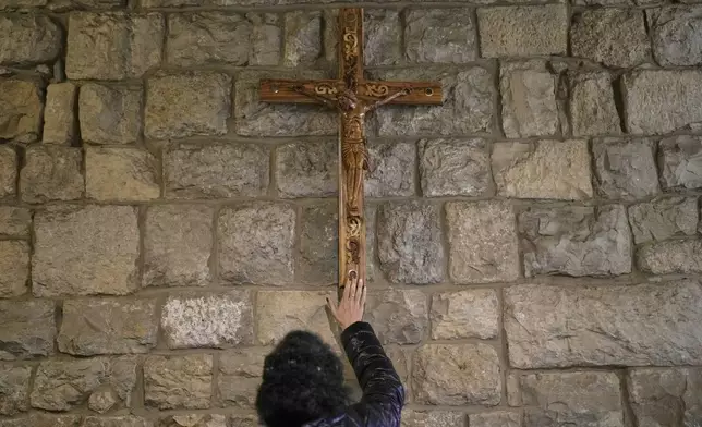 A worshipper touches a wooden crucifix inside the shrine of St. Charbel in the northern village of Annaya, Lebanon, Saturday, Nov. 15, 2025. (AP Photo/Hassan Ammar)