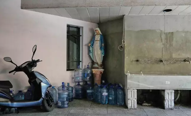 Large water jugs are stacked beside a statue of the Virgin Mary in the corner of a building in Beirut, Lebanon, Monday, Nov. 10, 2025. (AP Photo/Hassan Ammar)