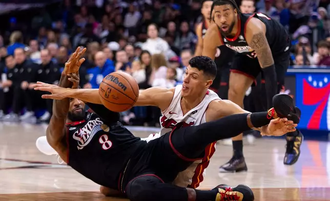 Philadelphia 76ers' Paul George, left, battles for the ball with Miami Heat's Simone Fontecchio, front right, during the first half of an NBA basketball game, Sunday, Nov. 23, 2025, in Philadelphia. (AP Photo/Chris Szagola)