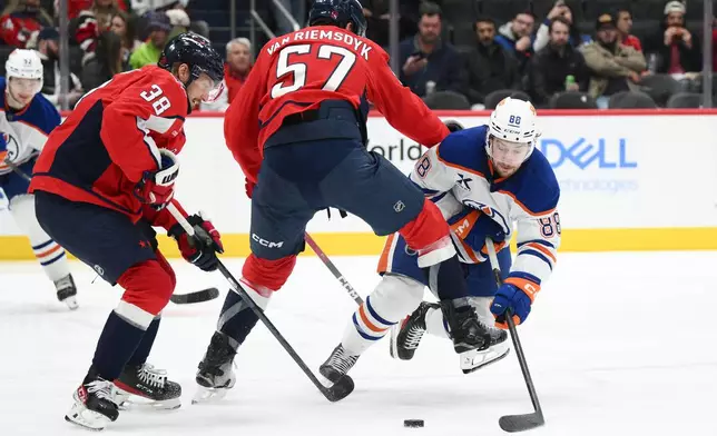 Edmonton Oilers left wing Andrew Mangiapane (88) lunges for the puck against Washington Capitals defenseman Trevor van Riemsdyk (57) and defenseman Rasmus Sandin (38) during the second period of an NHL hockey game, Wednesday, Nov. 19, 2025, in Washington. (AP Photo/Nick Wass)