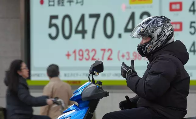 A person rides a scooter in front of an electronic stock board showing Japan's Nikkei index at a securities firm Thursday, Nov. 20, 2025, in Tokyo. (AP Photo/Eugene Hoshiko)