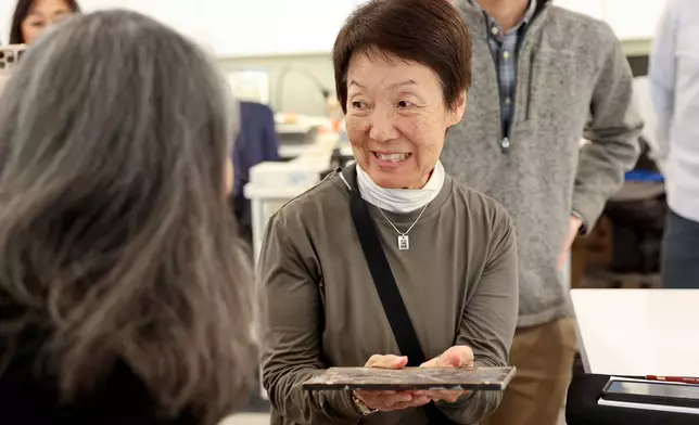 Karen Okawa, Japanese Church of Christ member and time capsule committee member, reacts as she holds a heavy lid that was used on the Japanese Church of Christ's 100-year-old time capsule at the University of Utah Marriott Library Preservation Department in Salt Lake City, Monday, Oct. 20, 2025. (Kristin Murphy/The Deseret News via AP)