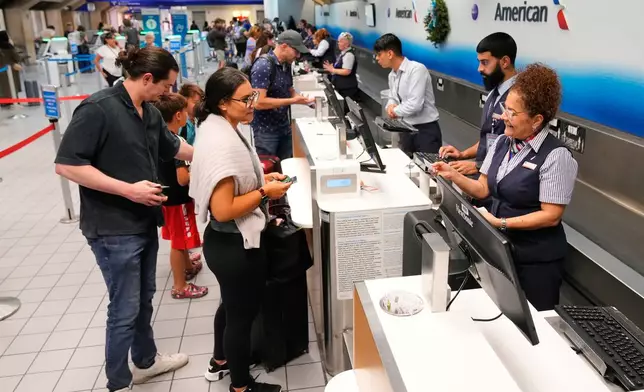 Myrna Santiago, right, a customer service agent with American Airlines, assists travelers at a ticketing gate at the Dallas Fort Worth International Airport, at DFW Airport, Texas, Friday, Nov. 21, 2025. (AP Photo/Tony Gutierrez)