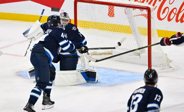 Winnipeg Jets' Josh Morrissey (44) clears the puck in front of goaltender Eric Comrie (1) after a Columbus Blue Jackets shot during the first period of an NHL hockey game in Winnipeg, Manitoba, Tuesday, Nov. 18, 2025. (Fred Greenslade/The Canadian Press via AP)