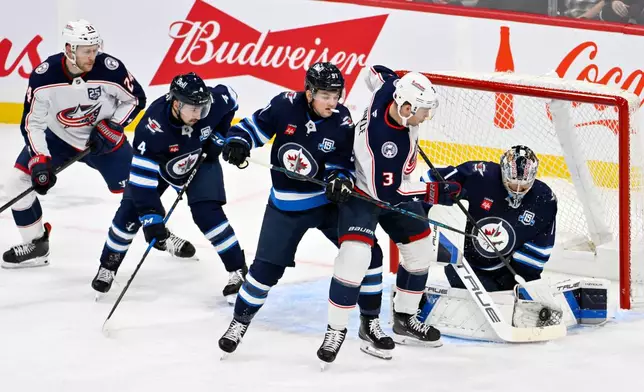 Winnipeg Jets goaltender Eric Comrie (1) makes a save on Columbus Blue Jackets' Charlie Coyle (3) as Cole Perfetti (91) helps defend during the first period of an NHL hockey game in Winnipeg, Manitoba, Tuesday, Nov. 18, 2025. (Fred Greenslade/The Canadian Press via AP)