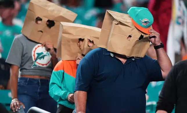 Miami Dolphins fans wear paper bags over their heads as they leave the stadium after a loss to the Baltimore Ravens in an NFL football game, Thursday, Oct. 30, 2025, in Miami Gardens, Fla. (AP Photo/Rebecca Blackwell)