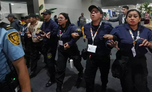 Officials form a chain to not allow attendees past after attendees were asked to leave the venue for the COP30 U.N. Climate Summit, Thursday, Nov. 20, 2025, in Belem, Brazil. (AP Photo/Andre Penner)