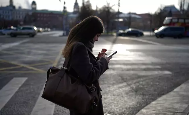 A woman looks at her smartphone in central Moscow, Russia, Thursday, Nov. 20, 2025. (AP Photo/Alexander Zemlianichenko)