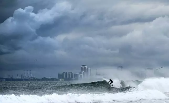 A surfer rides a wave as clouds gather above Bolsa Chica State Beach in Orange County, Calif., on Saturday, Nov. 15, 2025. (AP Photo/Noah Berger)