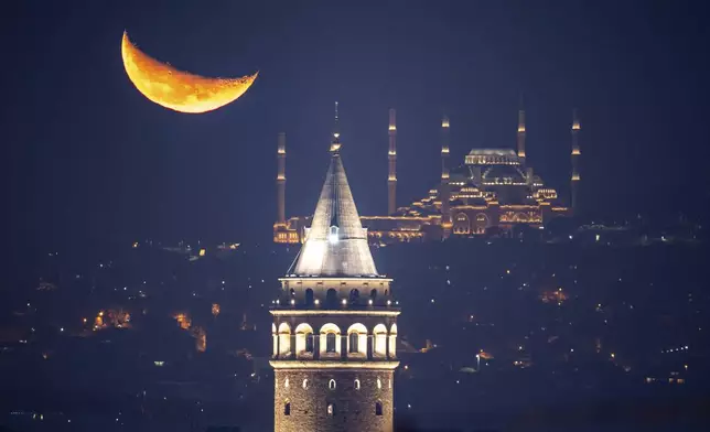 The crescent moon rises behind the Camlica mosque and Galata tower, in Istanbul, Turkey, early Friday, Nov. 14, 2025. (AP Photo/Emrah Gurel)