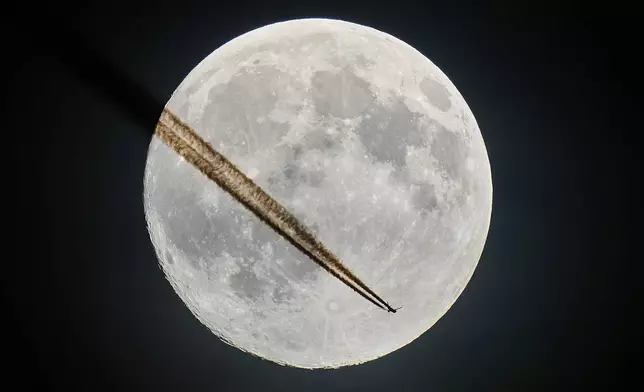 An aircraft passes the moon over Frankfurt, Germany, Tuesday, Nov. 4, 2025. (AP Photo/Michael Probst)