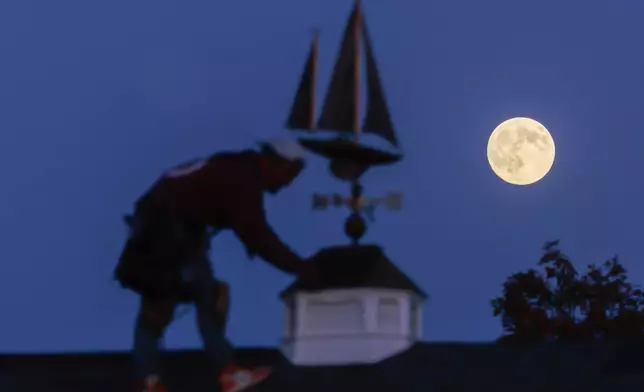 CORRECTS NOT YET A SUPERMOON The moon rises behind a roofing contractor working on a gazebo project in Oconomowoc, Wis., Tuesday, Nov. 4, 2025, before it becomes a Beaver Supermoon early Wednesday morning. (John Hart/Wisconsin State Journal via AP)